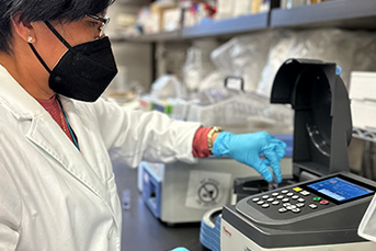 A woman in a lab touching a piece of equipment with a gloved hand
