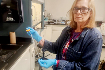 A woman with glasses holding an object with gloved hands