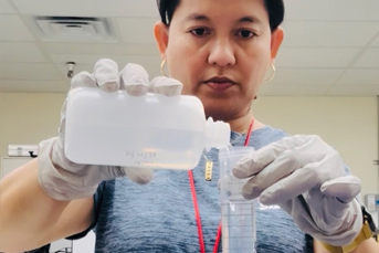 A woman transferring liquids in a lab with gloved hands
