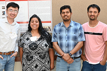 Four people facing the camera standing in front of an academic poster