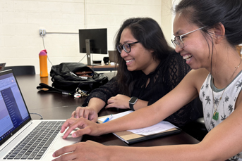 Two women smiling broadly while peering at a laptop screen