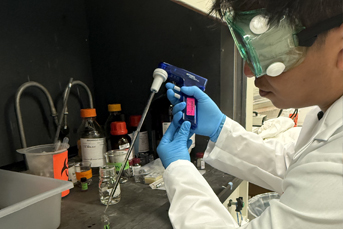A man wearing protective goggles standing in front of a vent hood in a lab 