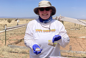 A woman wearing a hat and sunglasses, long sleeved white t-shirt and purple nitrile gloves at the Sevilleta field station near Socorro, New Mexico