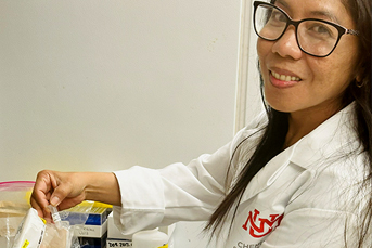 A woman in glasses and a UNM branded lab coat faces the camera